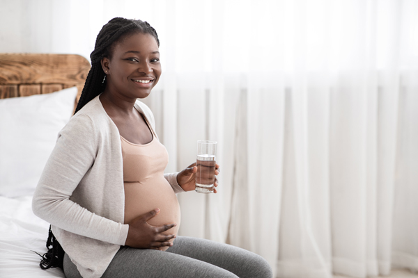 smiling woman sitting on bed with glass of water holding pregnant belly