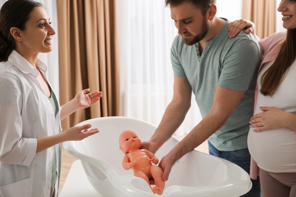 midwife showing new parents how to bath their baby using doll